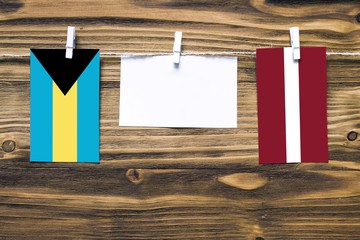 Hanging flags of Bahamas and Latvia attached to rope with clothes pins with copy space on white note paper on wooden background.Diplomatic relations between countries.