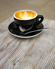 Cup of cappuccino with beautiful latte art on a wooden table with blurred background