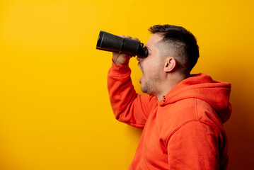 Handsome man with binocular on yellow background