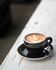 Cup of cappuccino with beautiful latte art on a wooden table with blurred background
