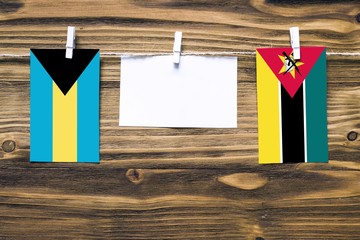 Hanging flags of Bahamas and Mozambique attached to rope with clothes pins with copy space on white...