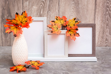 Ready Mock up. Three empty photo frames on a stand and a vase with orange maple leaves stand on the table. White-orange-beige color scheme. Copy space