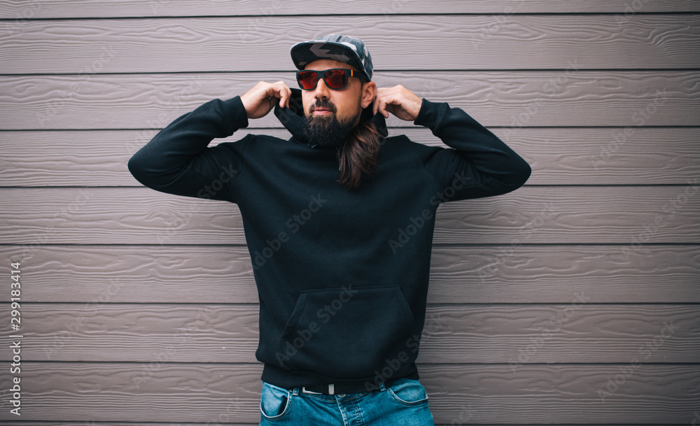 Wall mural City portrait of handsome hipster man with beard wearing black blank hoodie or hoody with space for your logo or design. Mockup for print - Wall murals