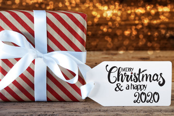 Fototapeta na wymiar One Christmas Gift With Label With English Calligraphy Merry Christmas And A Happy 2020. Wrapping Paper With A Bow And Lights In Background
