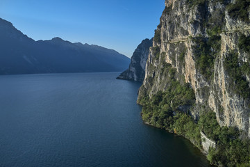 Rocks by the water. Panoramic view of Lake Garda, amid cliffs and alpine mountains. Autumn season.
