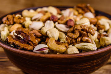 Various nuts (almond, cashew, hazelnut, pistachio, walnut) in ceramic plate on a wooden table. Vegetarian meal. Healthy eating concept