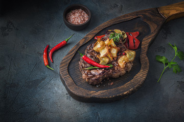 Juicy beef steak served on wooden board with crispy potatoe chips and chilli, close view