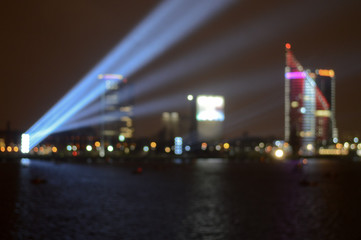 Fototapeta na wymiar long exposure, blurred background, night view of the city center and the river bay with festive lights, searchlight blue beams, a business center tower, night city life