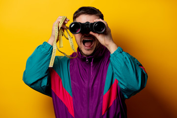Style man in 90s tracksuit with measuring tape and binoculars on yellow background
