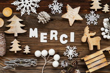 White Letters Building The Word Merci Means Thank You. Wooden Christmas Decoration Like Tree, Sled And Star. Brown Wooden Background