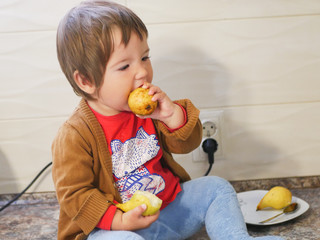 little child eats a pear. child boy eating fruits at a high stoic. in the kitchen.