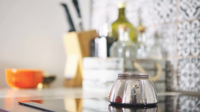4K person setting shiny metal moka pot on electric stove burner to make coffee, kitchen utensils and paraphernalia in background