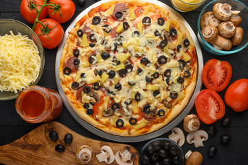 Pizza on a black background with ingredients, tomatoes, salami, mushrooms, sauce and mazzarella cheese. Italian pizza, culinary recipes concept, menu, restaurant, gourmet cuisine