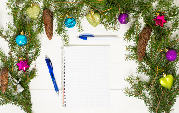 New Year's goals with colorful decorations and christmas tree branches on the white wooden table. Notepad with pens and Christmas decoration. Background photo with place for text.