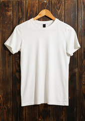 Hanger with blank white t-shirt on wooden background, space for text