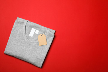 Folded blank grey t-shirt with tag on red background, space for text