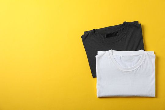 Folded blank t-shirts on yellow background, space for text - Powered by Adobe
