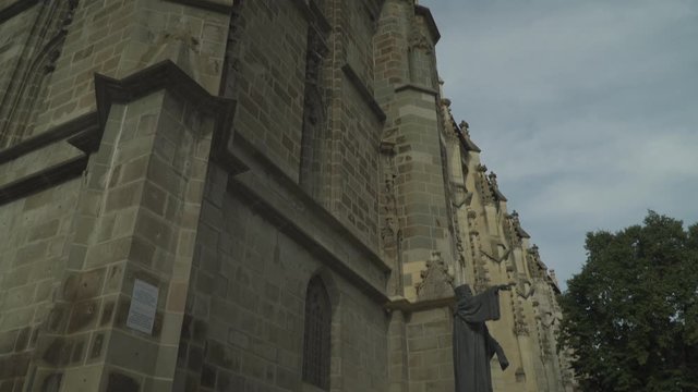 Majestic View Of The Black Church In Brasov, Romania With The Statue Of Johannes Honterus  Pointing Outside With A Tree, Sky And Clouds In Background - Tilt Down Shot