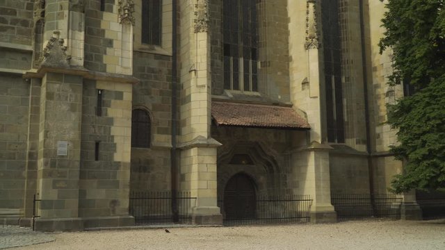 Front Exterior Of The Black Church In Brasov, Romania With Statue Of Johannes Honterus And Tree By The Entrance - Wide Panning Shot