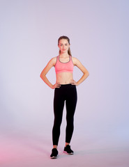 Young woman in full growth in fitness clothes standing on a pink purple background.