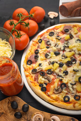 Pizza on a black background with ingredients, tomatoes, salami, mushrooms, sauce and mazzarella cheese.Italian pizza, the concept of culinary recipes, menu, restaurant, gourmet cuisine.Vertical frame