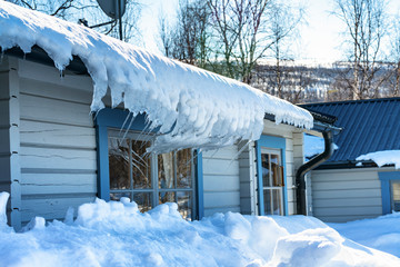 Photo of snow and bent icicles hanging from the roof of traditional swedish wooden light blue cabin...