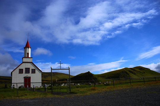 Iglesia blaca y roja en prado verde y cielo azul en Islandia