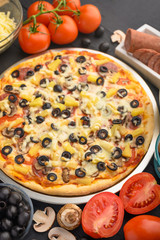 Italian pizza with ingredients on a dark background. Vertical photo.