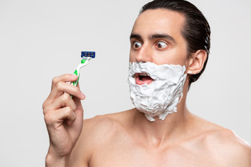 Handsome man with mustache uses shaving stick and shaving foam to trim his beard standning bare...