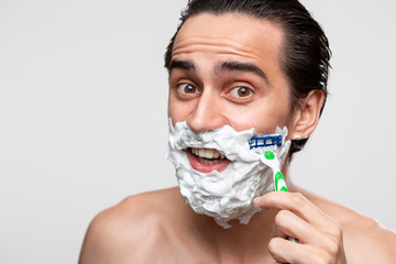Handsome man with mustache uses shaving stick and shaving foam to trim his beard standning bare...
