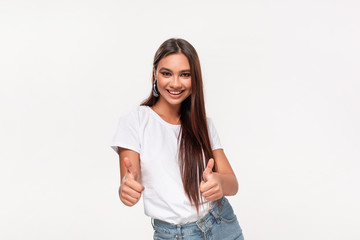 Excited pretty african-american teenager in a white t-shirt and blue jeans holding thumbs up  isolated over white background.