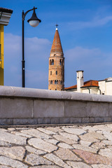 Protruding bell tower behind wall with blue sky in the background. Caorle Italy