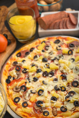 Pizza on a black background with ingredients, tomatoes, salami, mushrooms, sauce and mazzarella cheese.Italian pizza, the concept of culinary recipes, menu, restaurant, gourmet cuisine.Vertical frame
