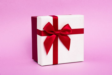 New Year's white gift with a red ribbon and bow on a pink background.