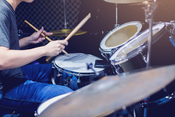 Young musicians wear t-shirts, jeans, and play the drum set and cymbals with wooden drumsticks in...