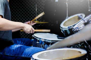 Young musicians wear t-shirts, jeans, and play the drum set and cymbals with wooden drumsticks in music room , the concept of musical instrument.