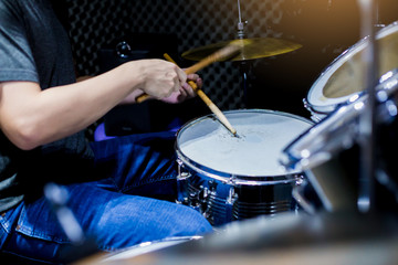 Young musicians wear t-shirts, jeans, and play the drum set and cymbals with wooden drumsticks in music room , the concept of musical instrument.