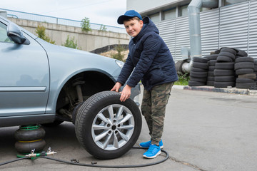 Fototapeta na wymiar Children's auto mechanic changes the wheel on a car. Replacing wheels on a car.