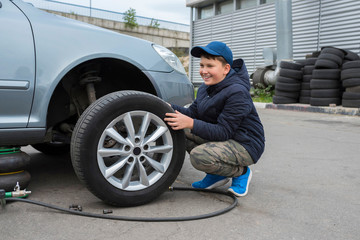 The boy helps at a car service. Replacing the wheels on the car, the jack holds the body in a raised position, with the wheel removed.