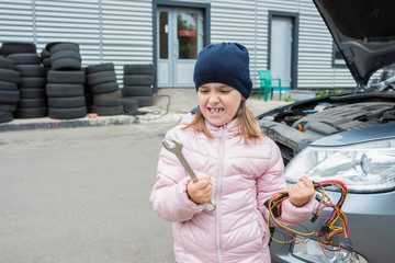 Emotional girl with a wrench and a bunch of wire, at a car service. Auto repair concept.