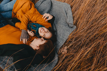 Young man and woman are lying and hugging on a plaid in an autumn field. Romance, traveling together, harmony, family happiness, a date in nature.