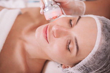 Obraz na płótnie Canvas Close up of a beautiful woman receiving facial rf-lifting treatment by beautician. Rejuvenation, pampering concept