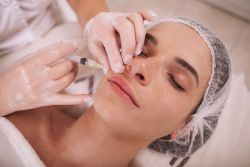 Young woman getting lip augmentation injections by professional cosmetologist. Beautician injecting...
