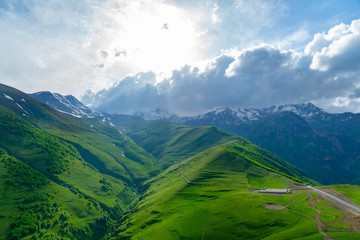 Fototapeta premium Landscape mountain view peaks in snow and green hills, deep blue sky and huge white clouds background, Caucasian mountains, Kazbek mountain