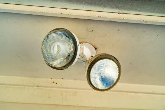 Old dilapidated flood light mounted on the soffit of a residential home in need of repair