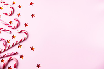 Pink background with christmas candy canes, shining red stars and copy space for your text