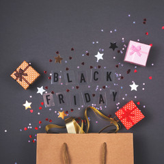 Kraft paper bag on bright dark background. With gift boxes and confetti. Black friday is written.