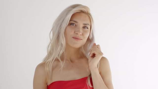 Chest-up shot of blonde Caucasian girl with bare shoulders and long hair putting two tabs of gum in mouth and chewing, while gazing seductively at camera and smiling