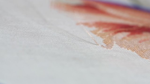 Woman hands doing cross-stitch of red flower. A close up of embroidery.