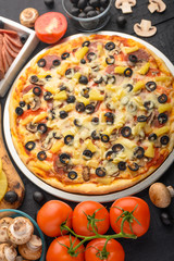 Pizza on a black background with ingredients, tomatoes, salami, mushrooms, sauce and mazzarella cheese.Italian pizza, the concept of culinary recipes, menu, restaurant, gourmet cuisine.Vertical frame
